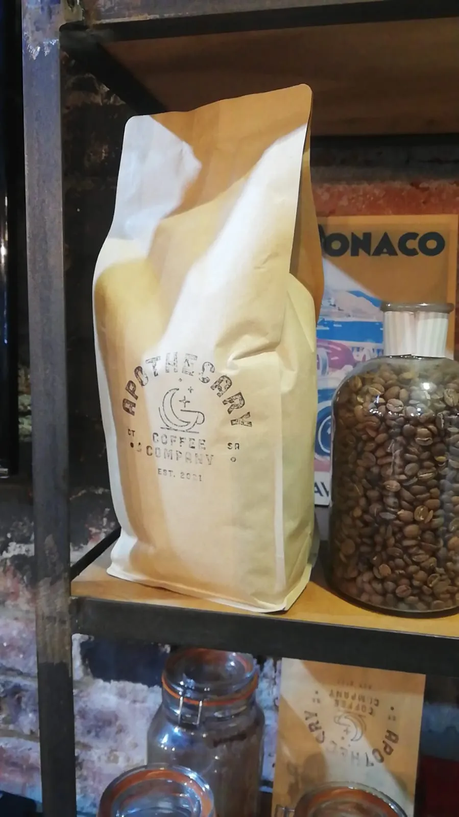 Apothecary Coffee bag on a shelf next to a large glass jar of green coffee beans inside the Laude cafe