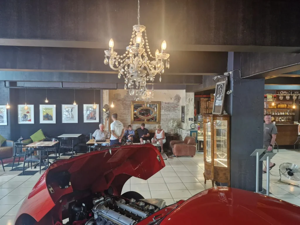 Interior of Crankshaft Cafe with a red Jaguar E-Type under a chandelier, patrons in the lounge beyond.