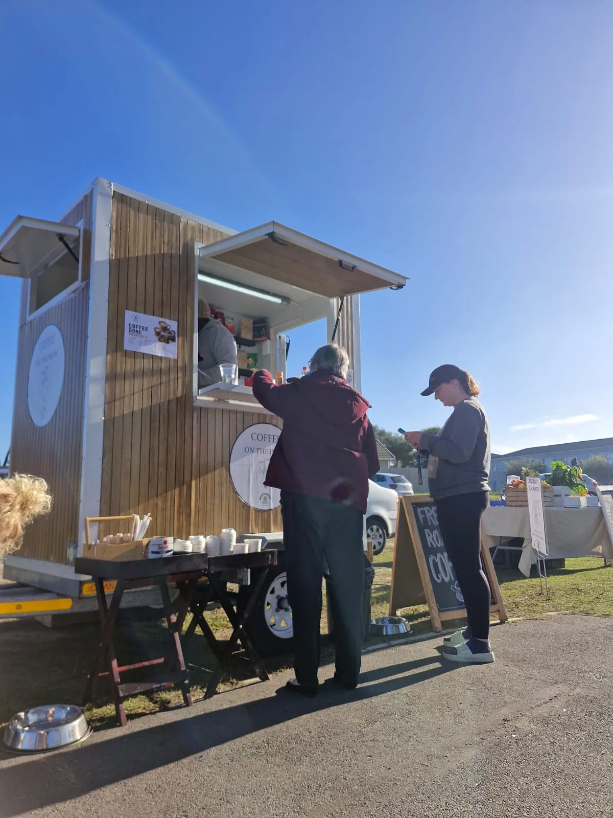 Apothecary Coffee trailer serving customers at the Echium Park Saturday market, with a Fresh Roasted Coffee chalkboard and market stalls