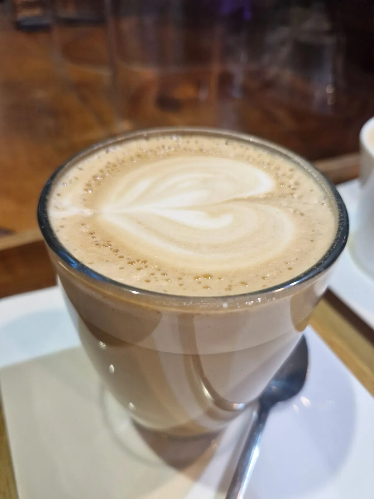 Glass cup of coffee with heart-shaped latte art on a saucer on a wooden cafe counter at Laude